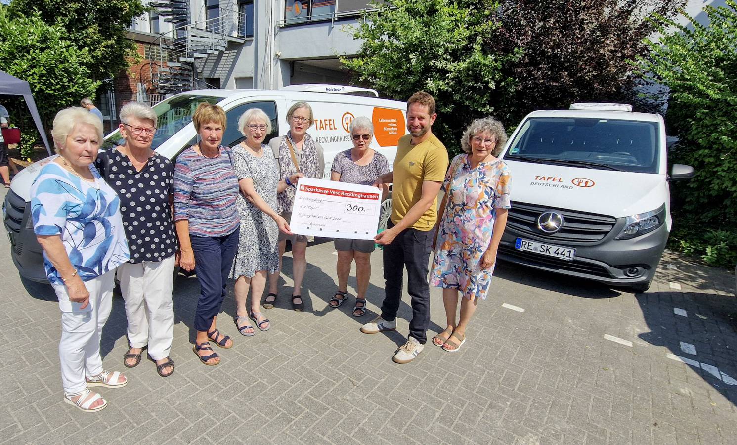 Frauen der kfd Pfarrei St. Antonius stehen mit Tafel-Koordinator Daniel Ruppert vor zwei Tafel-Fahrzeugen , zu sehen ist auch eine symbolscher Scheck, auf dem die Spendensumme 300 Euro eingetragen ist.